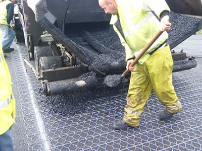 A worker is paving asphalt on the surface of hexagonal wire mesh, under the wire mesh is also a layer of asphalt.