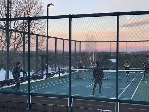 Several players are in the paddle tennis court enclosed by chicken wire.