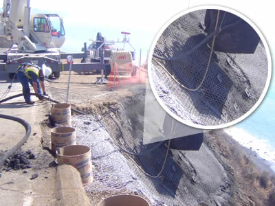 A cement gun is spraying cement on the suspended and overlapped hexagonal wire mesh netting on mountain top.