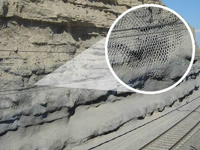 A railway road extends itself besides a hexagonal wire mesh netting suspended slope.