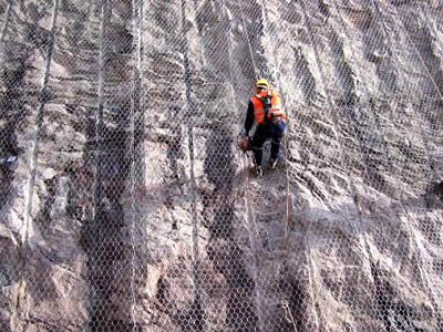 Workers are hanging hexagonal wire mesh on the surface on the mountain.