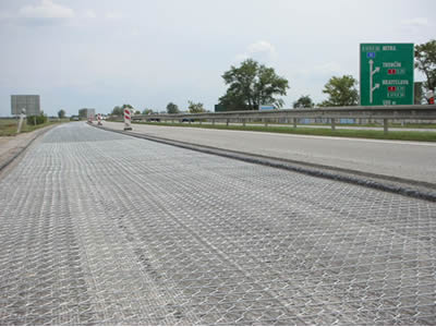This is a road with the left half paved with hexagonal wire mesh, the right half have finished asphalt paving project.