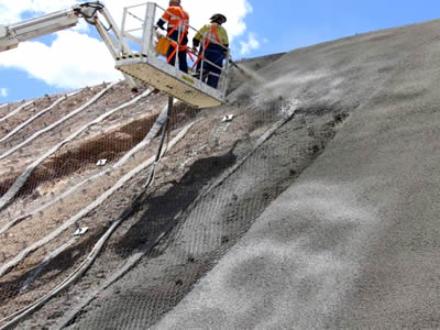 Workers are spraying concrete onto the hexagonal wire mesh netting.
