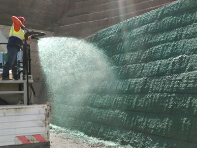 A worker who is standing on a white car is spraying seeding on to the surface of our green terramesh product.