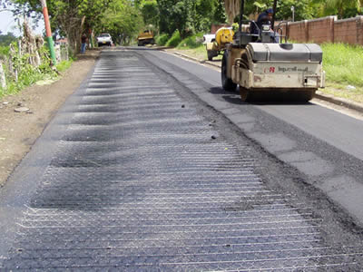 The left part of a track is paved with hexagonal wire mesh, the right part is being rolled by a car after the asphalt applying is finished.