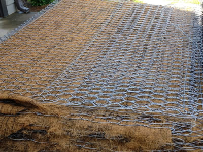 Several trapezoidal gabion baskets are lying on the ground.