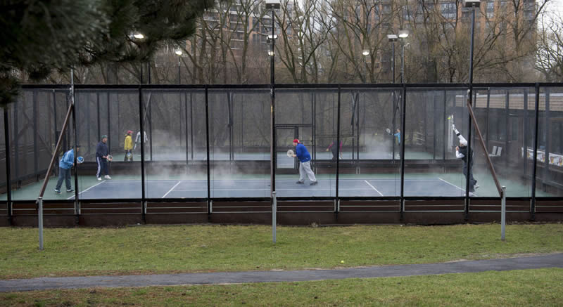 Two individual paddle tennis courts are adjacent with each other. People are exercising in winter with warm stem erupted.