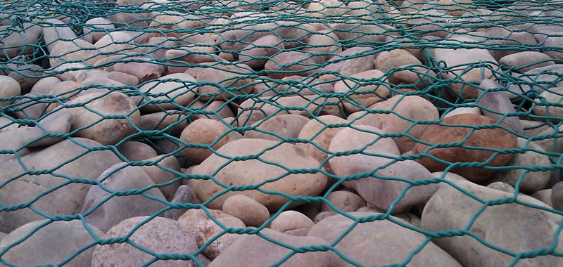 The picture shows many green PVC gabion baskets filled with stones or empty.