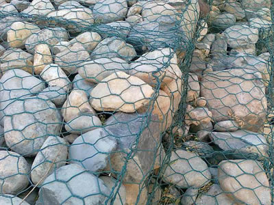 Green PVC coated gabion mattresses are filled full of stones.