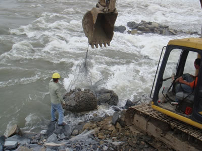 An excavator is placing a bag of rocks on the river bank.