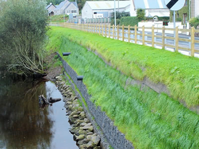Beneath the road is a small river, on the flank of the road is trapezoidal gabion basket and grass on the surface of it.