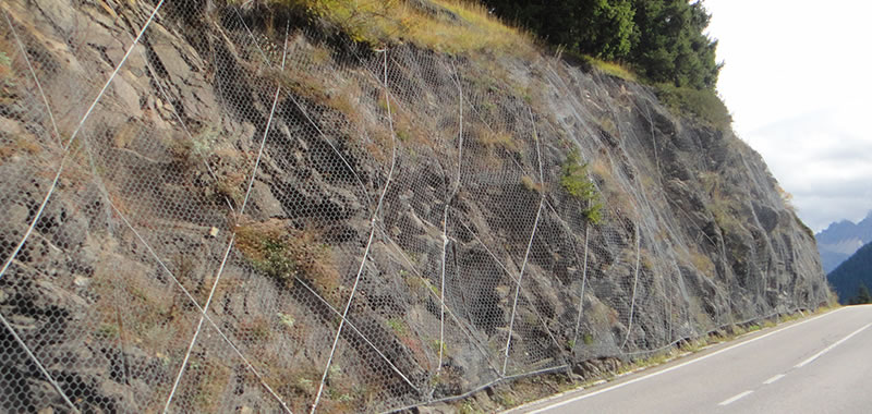 Rockfall netting hangs on the slope with the rock bolts fixing the hexagonal mesh beside the road.