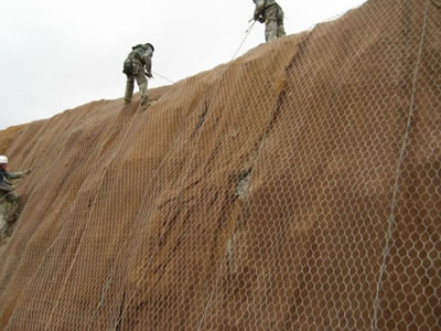 Three people are installing rockfall netting on cliff.