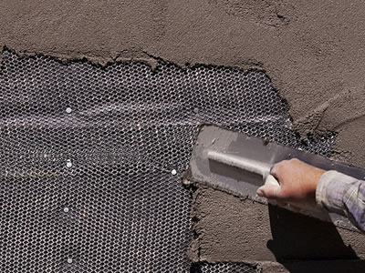 Stucco mesh is tiled on the wall and a man is wiping plaster on it.