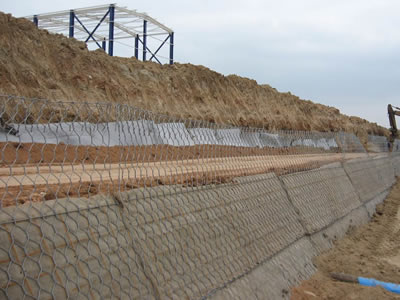 An array of green hexagonal terramesh is fixed, compactor is preparing to rolled fill.