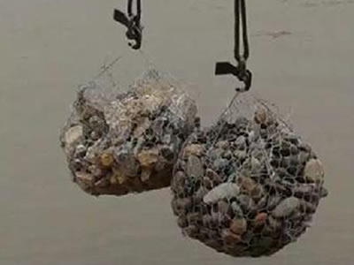 Two hooks are hanging two bags of rocks on the top of river.