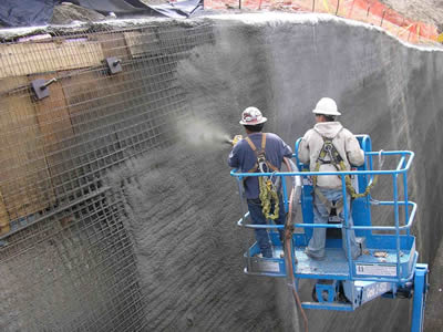 Two workers are standing on a blue work platform to spray concrete on a welded wire mesh reinforced slope.